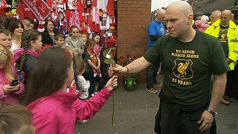 A walker hands a red rose to a child at the Anfield memorial