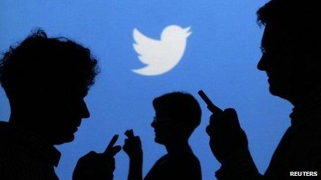 People holding mobile phones in front of the Twitter logo (27 September 2013)