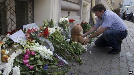 A man lays a stuffed bear among flowers outside the Dutch embassy in Moscow