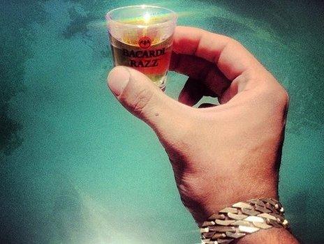 A hand holding a shot of what appears to be rum, with an expensive looking bracelet on their wrist