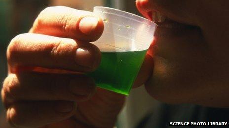 A close-up of someone drinking a small container of green liquid - methadone