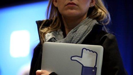 woman holds laptop with Facebook "like" sticker on it