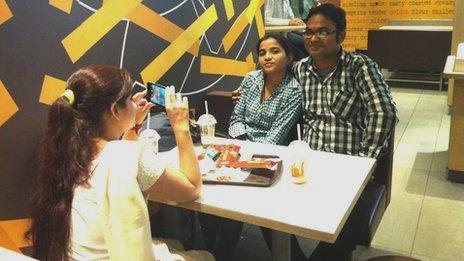 A young couple have their picture taken at a McDonald's restaurant by a friend on her phone