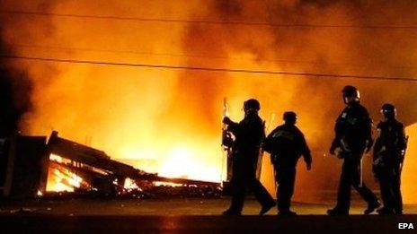 Police in riot gear walk past a burning building in Ferguson, Missouri