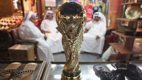 Arab men sit at a shoemaker's stall with a replica of the FIFA World Cup trophy in the Souq Waqif traditional market