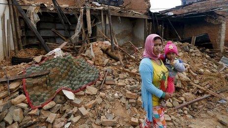 A Nepali woman holds her baby in front of the wreckage of a house that was completely destroyed in Saturday's earthquake in Gorkha, Nepal (30 April 2015)