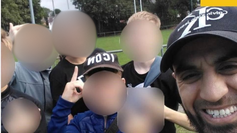 A man wearing a cap takes a selfie with a group of young people, and another adult, whose faces are all blurred