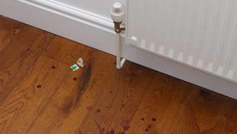 A white radiator above a wooden floor spattered with blood