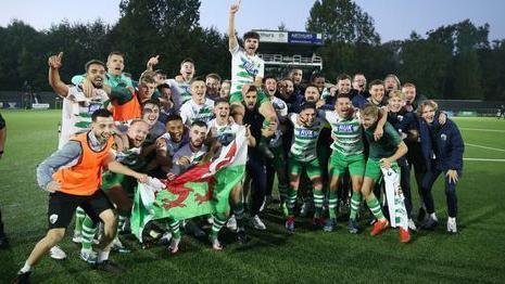 TNS players celebrate in front of a Welsh flag