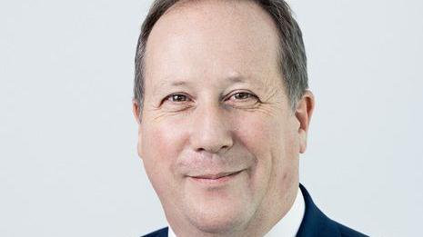 A man smiling into the camera. He has dark hair that is slightly greying.