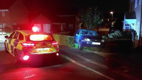 Police car parked next to blue car in hedge