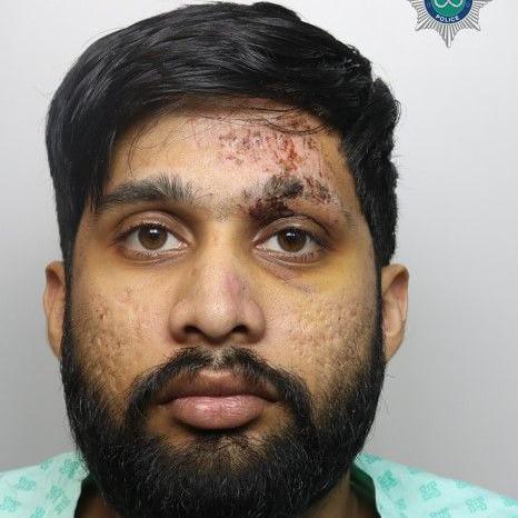A mugshot of a man with black hair and a black beard. He is wearing a light green-coloured shirt.