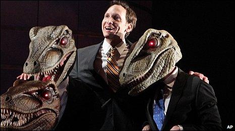 Stephen Kunken perform with actors wearing raptor masks in Enron