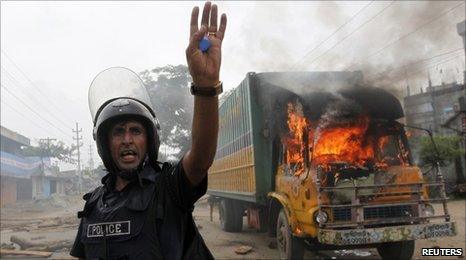 Policeman calls his comrades for help in front of a truck burnt by garment workers in Ashulia