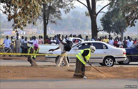 People gather across a street at one of the scenes of Sunday's bomb blasts in Kampala