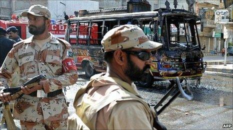 Pakistani soldiers in Karachi patrol the area around a minibus torched by protesters, following the murder of Imran Farooq