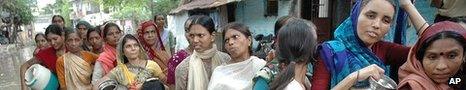 Women stand in floodwaters to collect drinking water in India