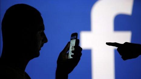 Man holding a phone in front of the Facebook logo