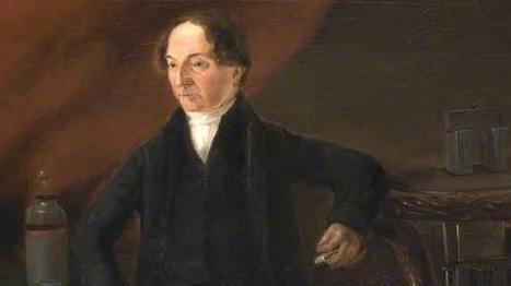 A painting of a Georgian gentleman with short dark hair parted in the middle. He wears a frock coat and waistcoat and leans his elbow on a high table.