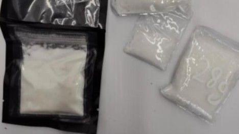 Sachets of the white powdered drugs on a white table. One of the sachets says 28 grams.