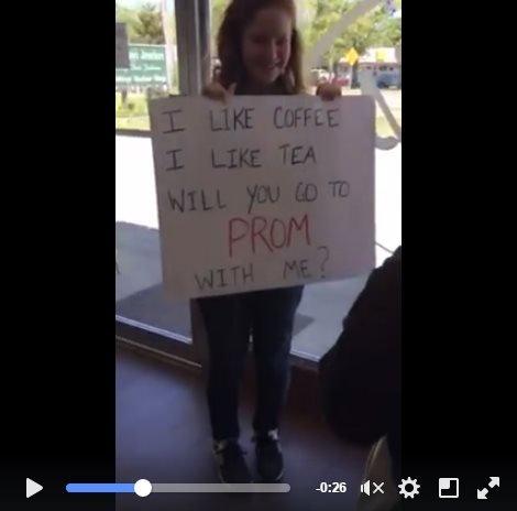 Still image of Lillie asking Trevor to prom with a sign that reads: "I like coffee, I like tea, will you go to prom with me?"