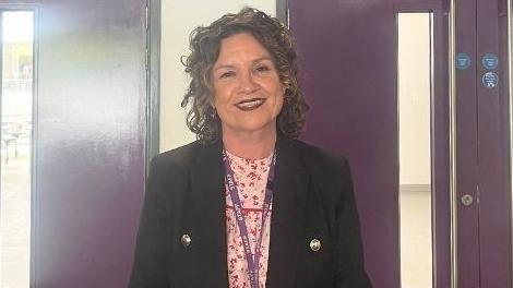 A woman is smiling near two sets of purple double doors.