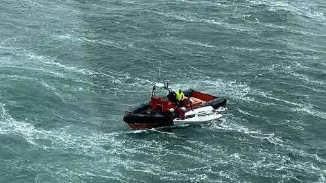 Lifeboat with white dinghy close to its side in choppy seas.