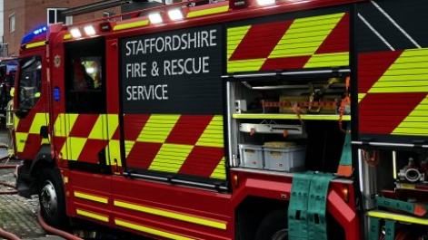 The side of a red fire engine, some of the compartments are open, and pipes  trail on the ground. Staffordshire Fire and Rescue Service is written on the side of the vehicle