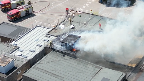 An aerial photograph taken above Ormiston Cliff Park Primary  Academy in Gorleston. Smoke is billowing out from the roof of the building. There are fire fighters on the roof trying to extinguish the flames.
