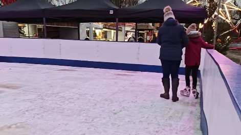 A parent and a child skating on a plastic ice rink