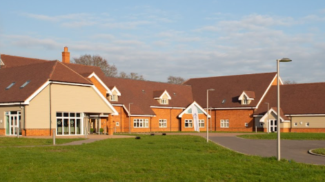 The red brick and beige cladded building of the hospice with greenery outside the front.