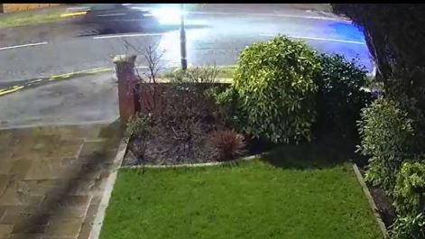 A still from doorbell video footage shows a blurry image of a dark coloured car driving along the road, with a garden and driveway seen close to the camera.