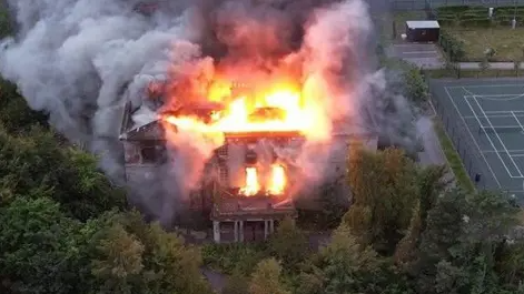 The manor house with flames billowing from the roof.