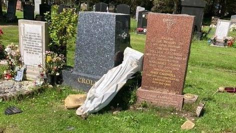 An upturned statue lies between two other headstones