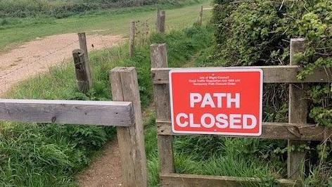A red "path closed" sign affixed to a wooden fence, possible a stile, by a field.