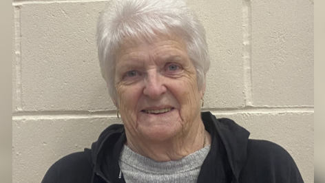 A lady with white hair in a grey jumper wearing a black hoodie. 