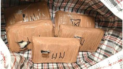 Tightly packages of cocaine are placed into a tartan-style bag for life. Three of the five packages have been busted open to show a white powder coming out of it