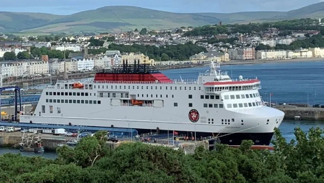 The Manxman, which is a large ferry in the Steam Packet's colours of white, red and black, moored in Douglas Harbour with the Douglas Bay and the promenade in the background.