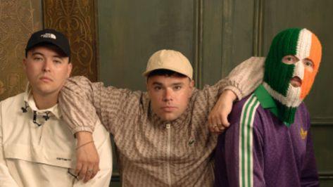 Three men are posing for a photo. Two are wearing caps and one is wearing a green, white and orange balaclava.