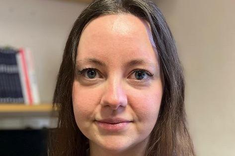Nikki Rutter is pictured in her office with book shelves behind. She has long dark hair and blue eyes.