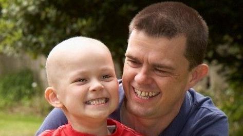 A young child smiling next to a man with brown hair.
