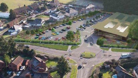 Birdseye view of proposed site, a CGI mock up of the store, which has solar panels on the roof, with a car park and residential streets surrounding the shop, with a roundabout