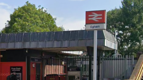 A Google Street image of the outside of Egham Railway Station. There is a sign with the railway logo and the word "Egham" under it.