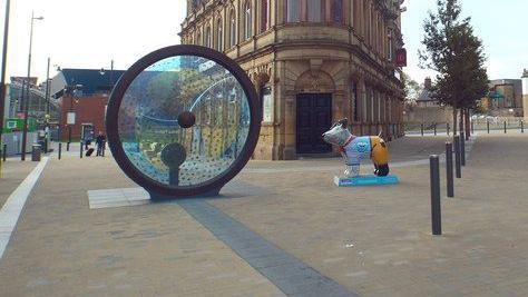 The Propellers of the City artwork in Sunderland's Keel Square. It is a blue and yellow glass circle in a grey frame. It can be rotated like the steering wheel of a boat.