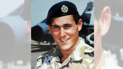 Mark Shephard - a smiling man in uniform looking at camera with military aircraft in the background 