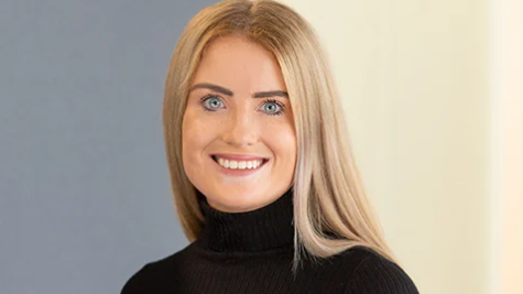 Simone White, who has long straight blonde hair and wears a black polo neck jumper, smiles at the camera in a work headshot