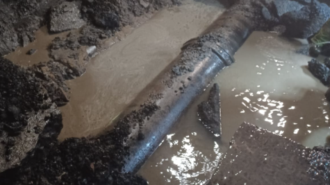 A large pipe underground submerged in muddy water