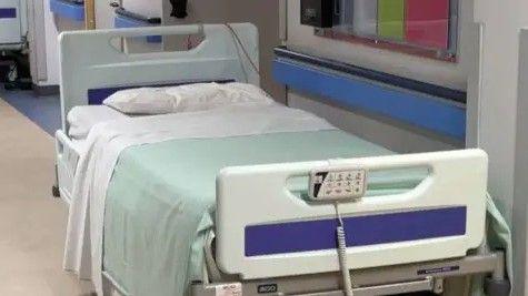 A hospital bed, which has white pillows and sheet and a pale green blanket on it.