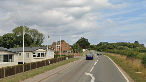 A view of the road with a caravan site to the left.  It is summer in the picture and the sun is shining.