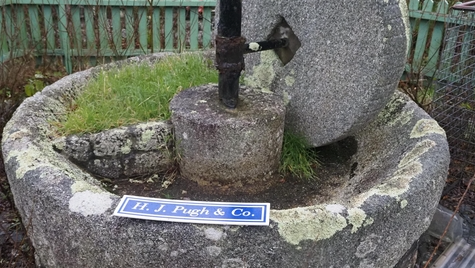 A stone mill with a stone tub and an upright wheel above it and a metal axle.